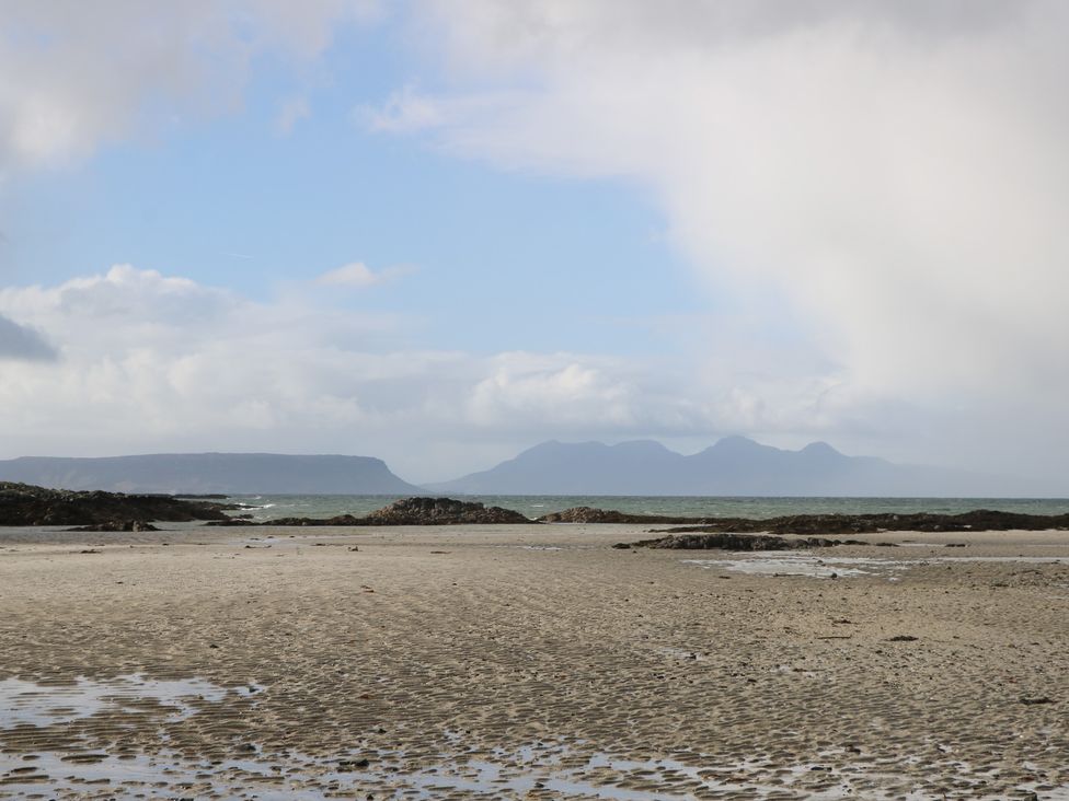 A beachscape with sand, rocks, and mountains in the distance at Island View Lodge Back of Keppoch near Arisaig