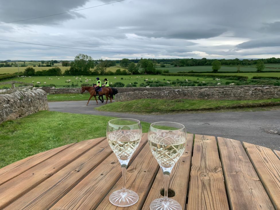 Two glasses on a table with horses riding in a field at Peace Cottage in Langton near Gainford