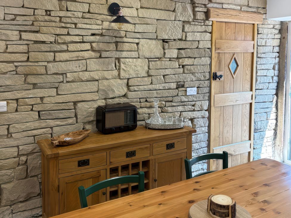 A dining room with a stone wall and wooden furniture at 12 Queen Street in Keighley
