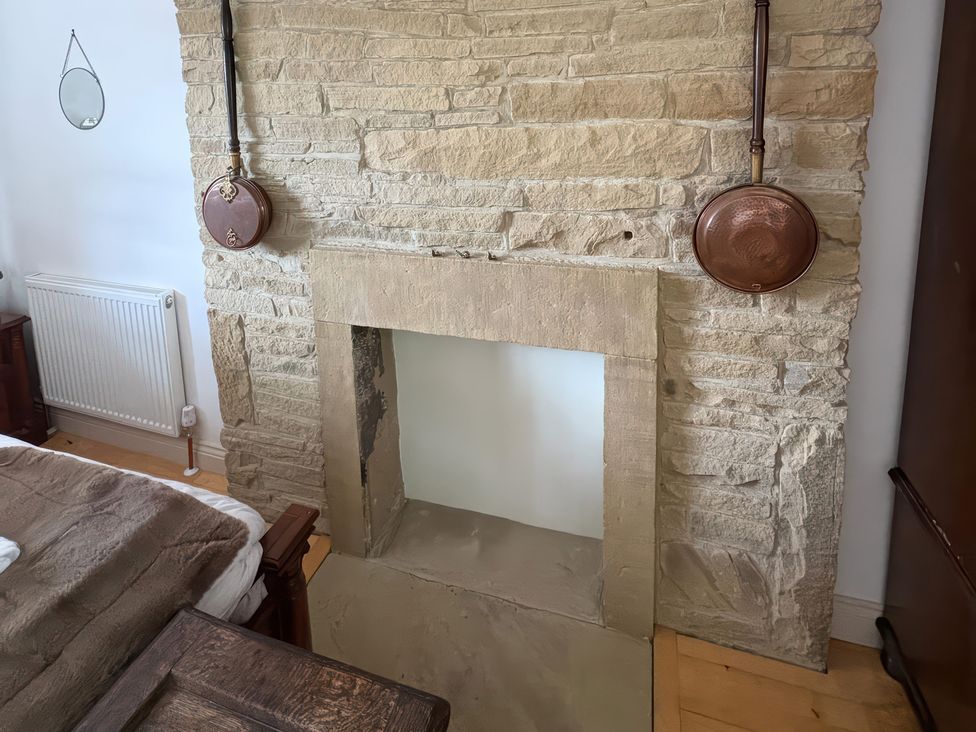 A stone fireplace with copper pans in a bedroom at 12 Queen Street in Keighley