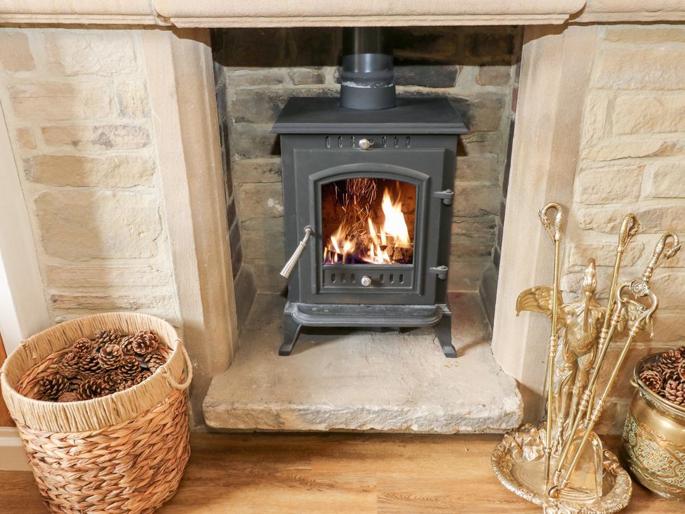 A fireplace with a wood stove and a basket of pinecones at Hivewood Cottage in Haworth