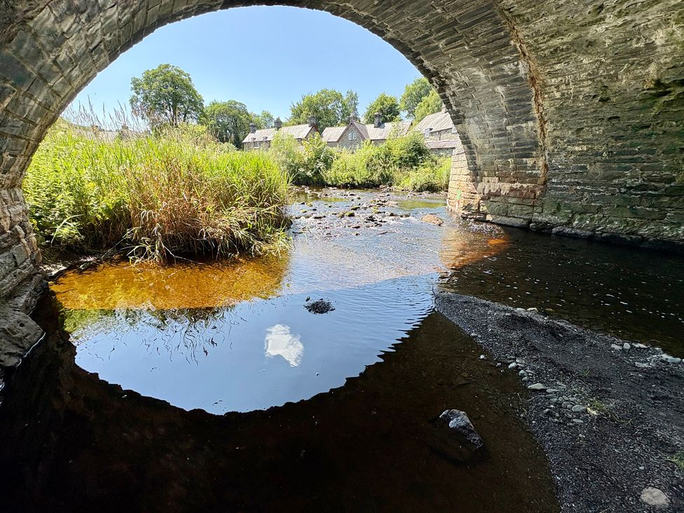 A view of a river under a stone bridge with grass and houses at Gwynfa Ysbyty Ifan
