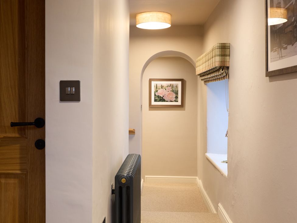 A hallway with a door, light fixture, radiator, window, and picture frame at Butler's Quarters in Matlock