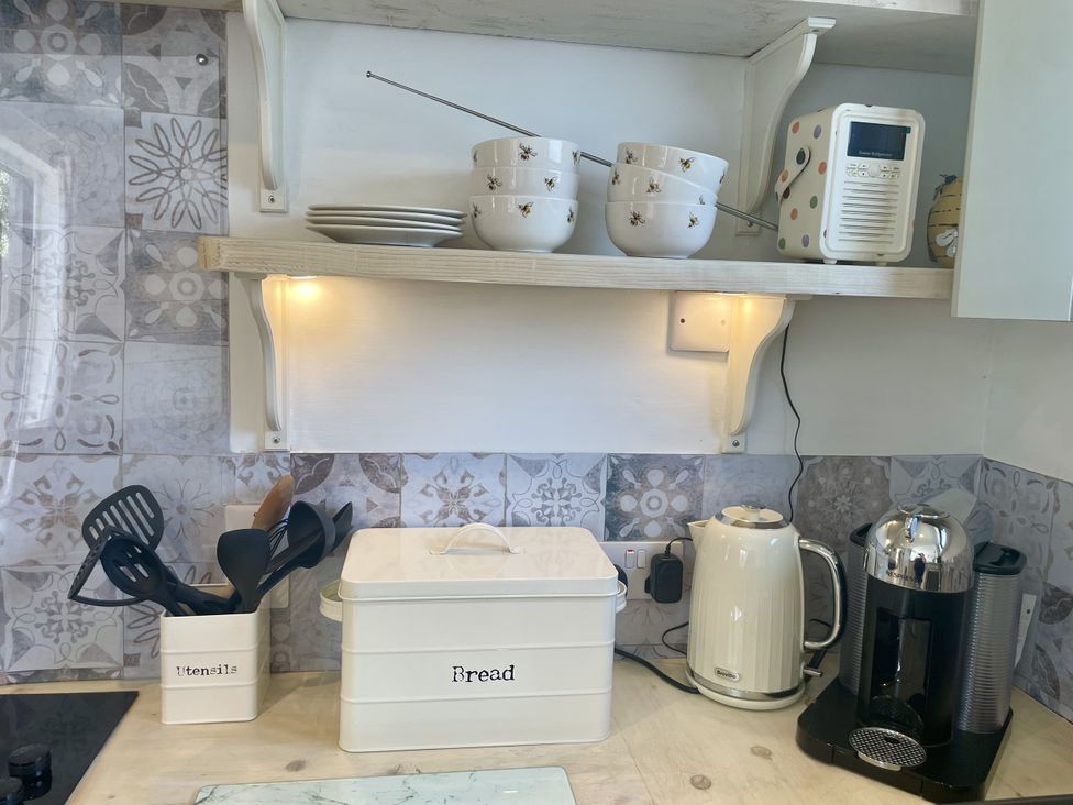 A kitchen with shelving, bowls, utensils, a kettle and a coffee machine at The Cow Shed in Mawgan Porth