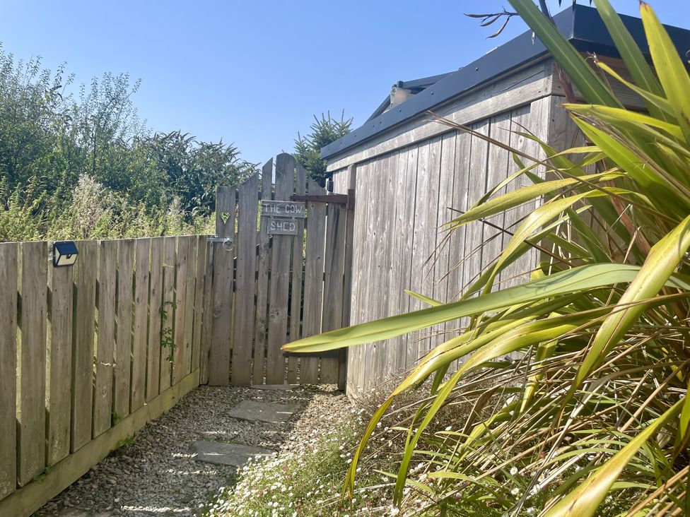 A gated entrance with a gravel path and plants at The Cow Shed in Mawgan Porth