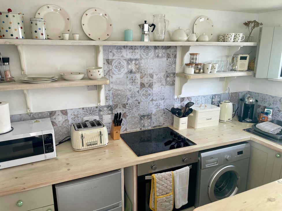 A kitchen with appliances and dishes on shelves at The Cow Shed in Mawgan Porth