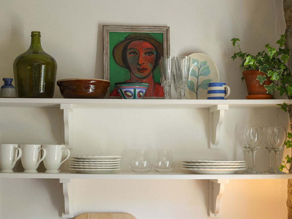 A kitchen shelf with dishes and glasses at Kittiwake in Newlyn