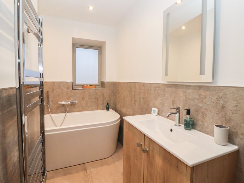 A bathroom with a bathtub, sink, and mirror at Stable End Cottage, York