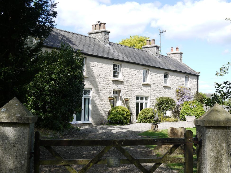 A stone house with multiple chimneys behind a wooden gate and garden at 1 The Green in Silverdale