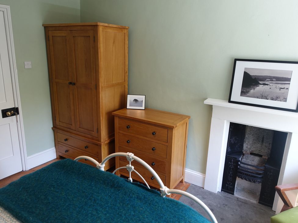 A bedroom with wooden furniture including a wardrobe and chest of drawers next to a fireplace with a framed photo on the mantel at 1 The Green in Silverdale