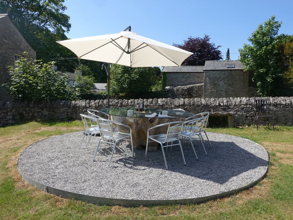 An outdoor seating area with a round glass table and metal chairs under a large white umbrella on gravel at 1 The Green in Silverdale