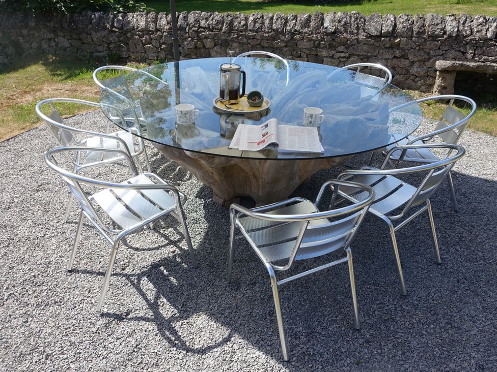 An outdoor round glass table with six metal chairs on a gravel surface with a stone wall in the background at 1 The Green in Silverdale