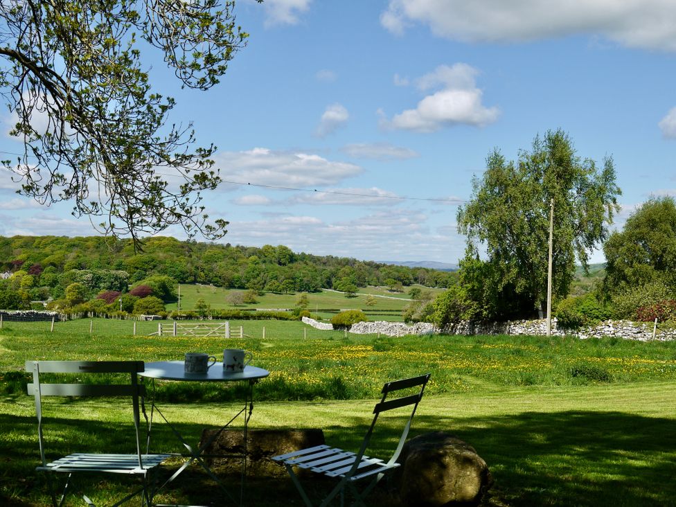 A garden with a table and two chairs overlooking a field with trees and a stone wall at 1 The Green in Silverdale