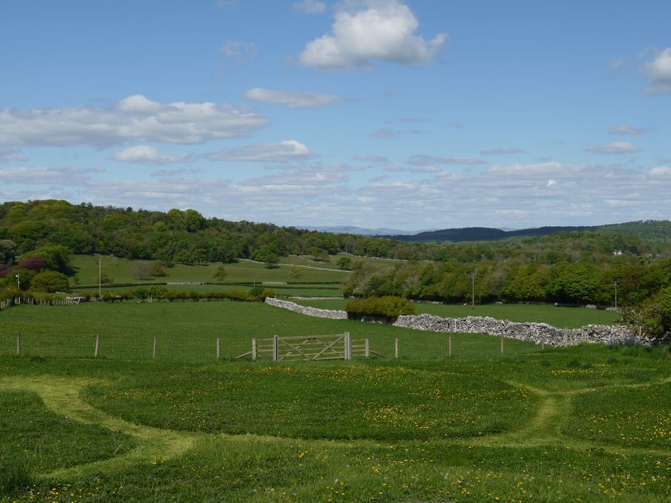 A rural field with a wooden gate stone walls and trees under a blue sky at 1 The Green in Silverdale