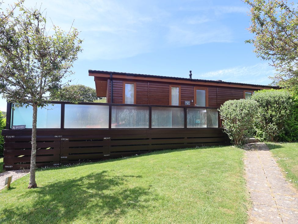A cabin with a balcony surrounded by grass and trees at Skyview in Newton Ferrers