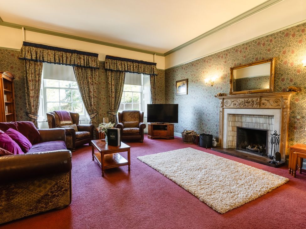 A living room with a sofa, armchair, coffee table, and television at Cheviot Manor in Akeld near Wooler