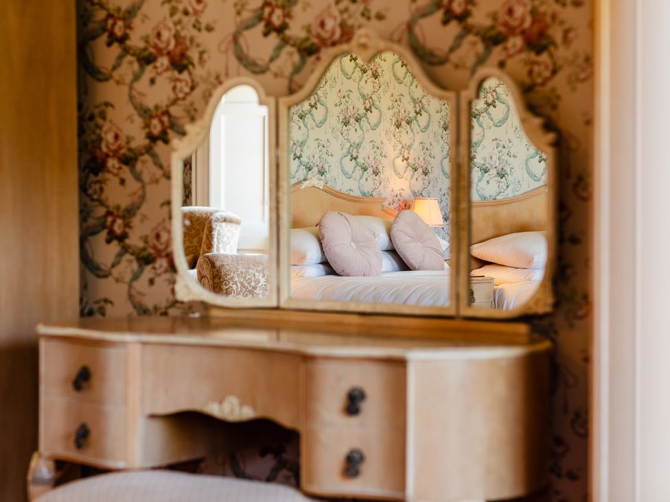 A dressing table with a mirror reflecting a bed at Cheviot Manor in Akeld near Wooler