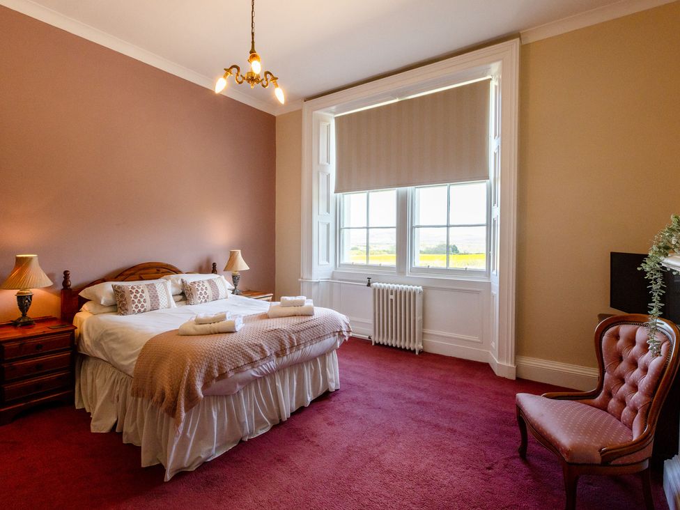 A bedroom with a bed, nightstand, lamp, and windows at Cheviot Manor near Wooler