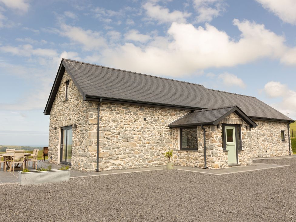 A stone building with a slate roof and patio table at Golygfa Cwrt in Talybont