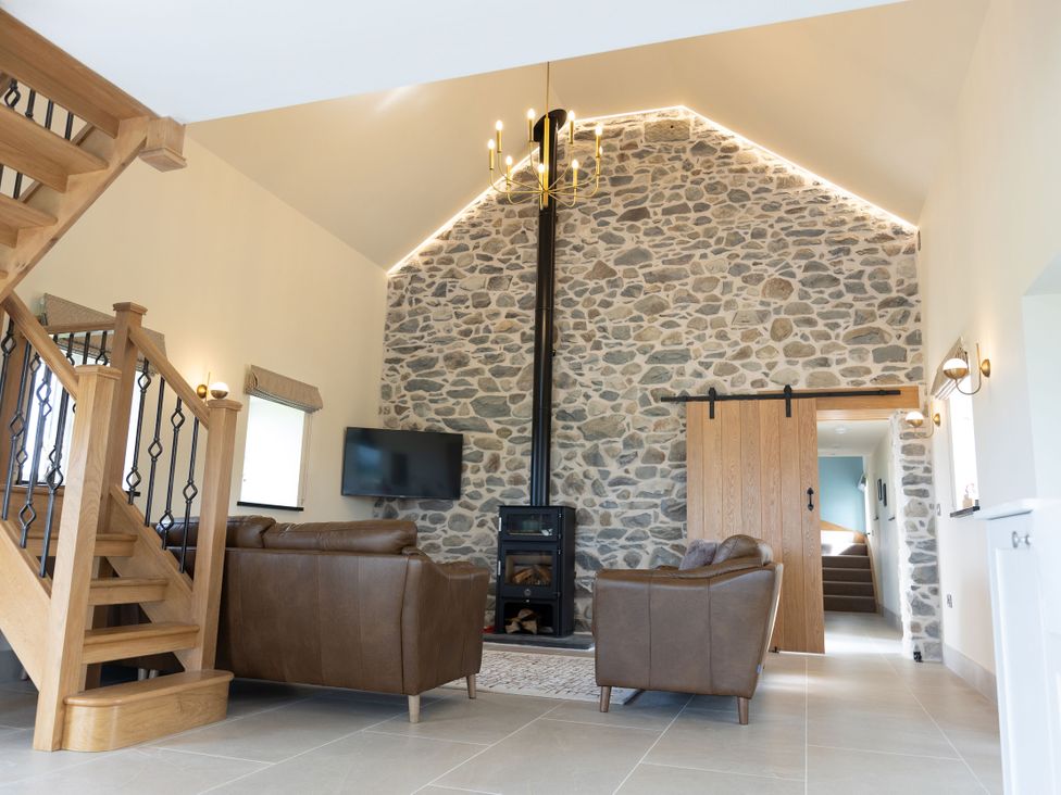 A living room with a stone wall and wooden staircase at Golygfa Cwrt Talybont