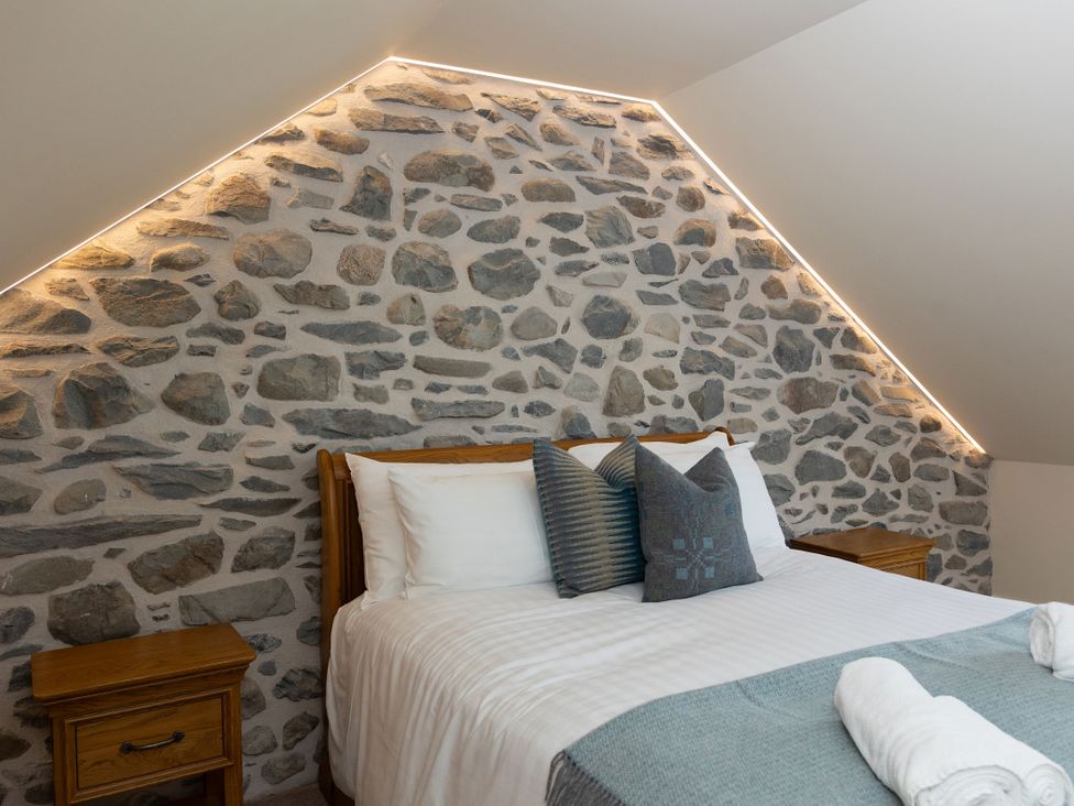 A bedroom with a bed and stone wall at Golygfa Cwrt in Talybont