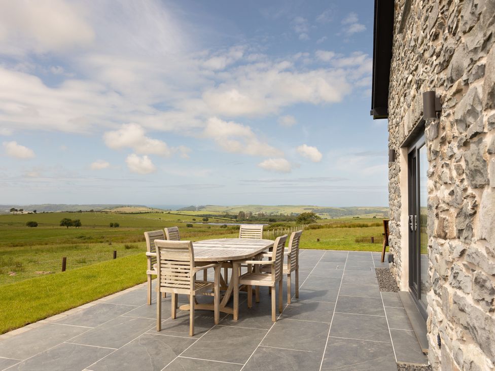 A patio area with a table and chairs overlooking the countryside at Golygfa Cwrt in Talybont
