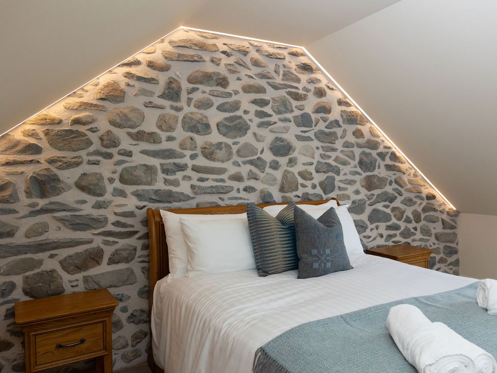 A bedroom with a stone wall and wooden furniture at Golygfa Cwrt near Bontgoch and Penrhyncoch