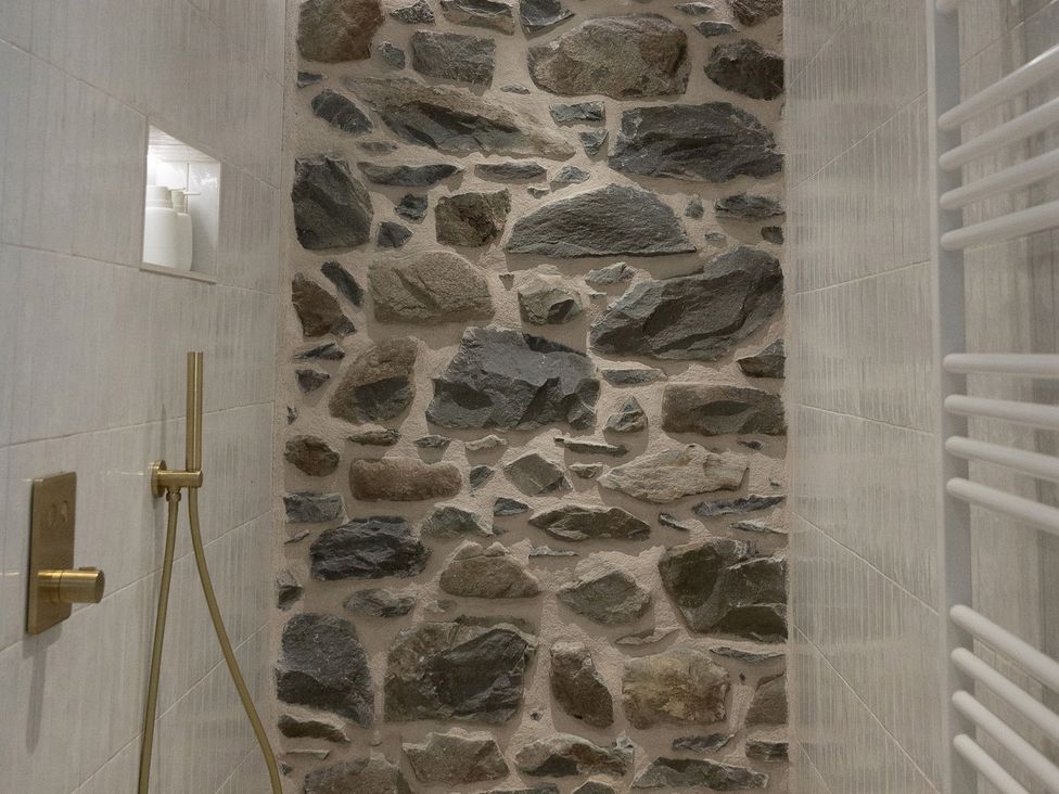 A shower area with a stone wall and plumbing fixtures at Golygfa Cwrt near Bontgoch and Penrhyncoch