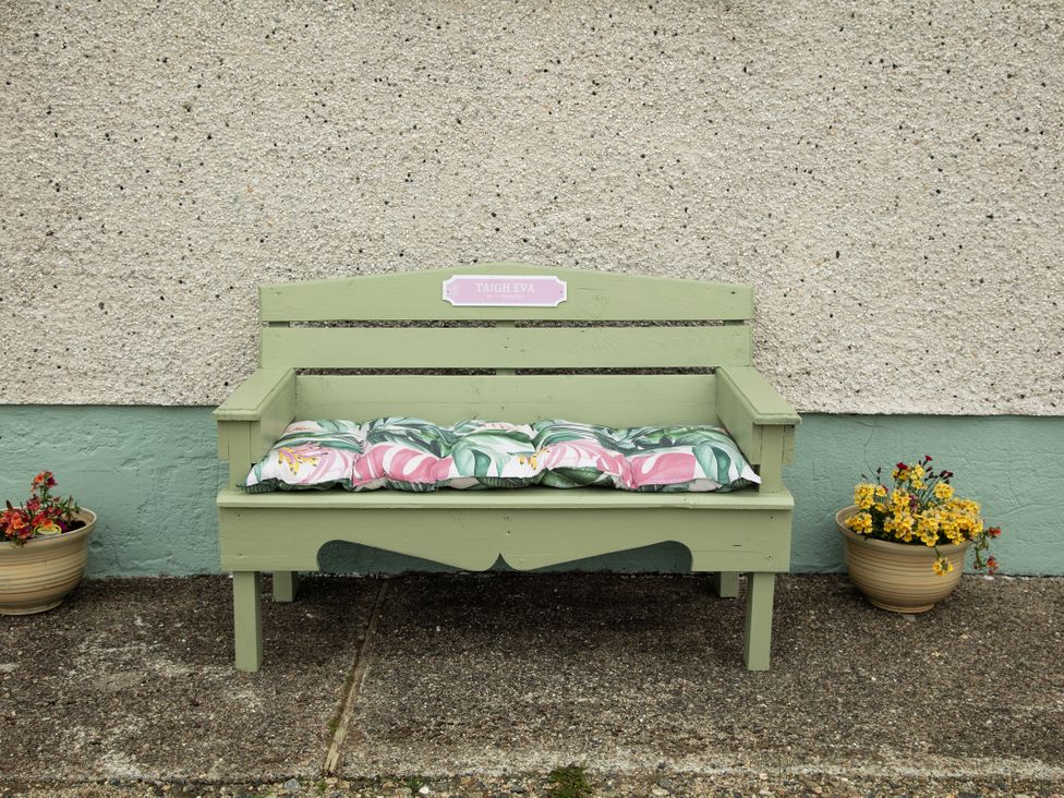 A green bench with cushions and flower pots at Taigh Eva near Lochmaddy
