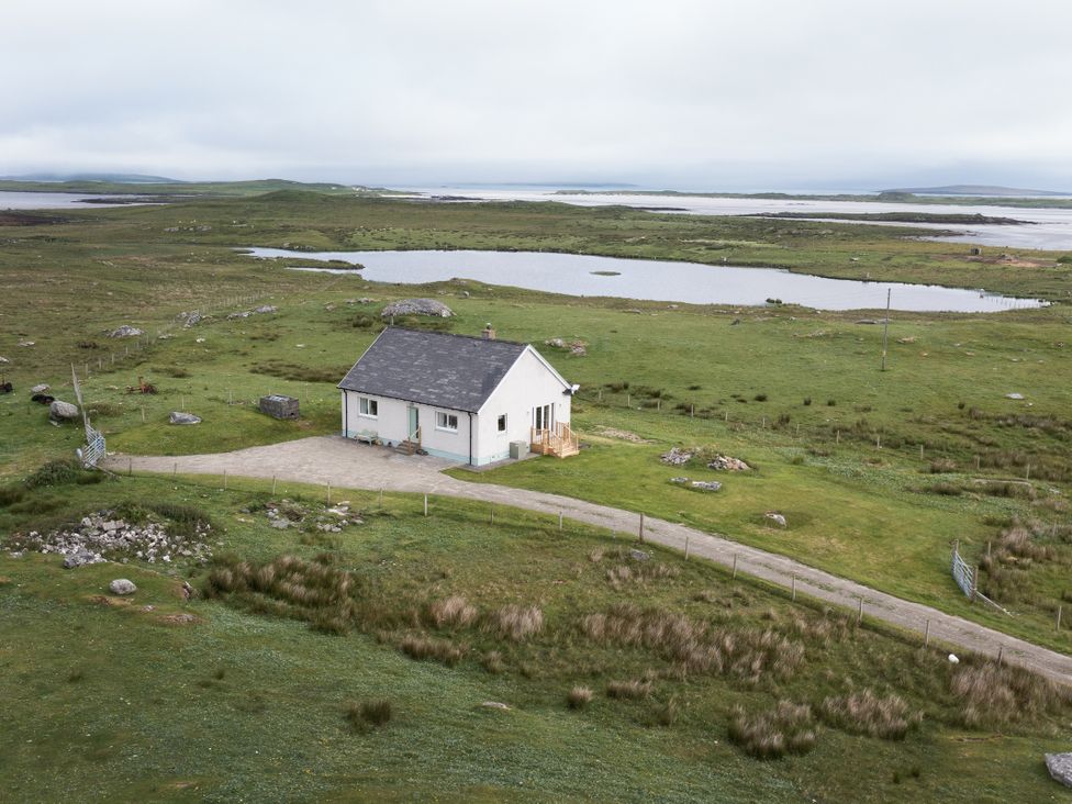 A house by a lake with a road leading to it at Taigh Eva near Lochmaddy