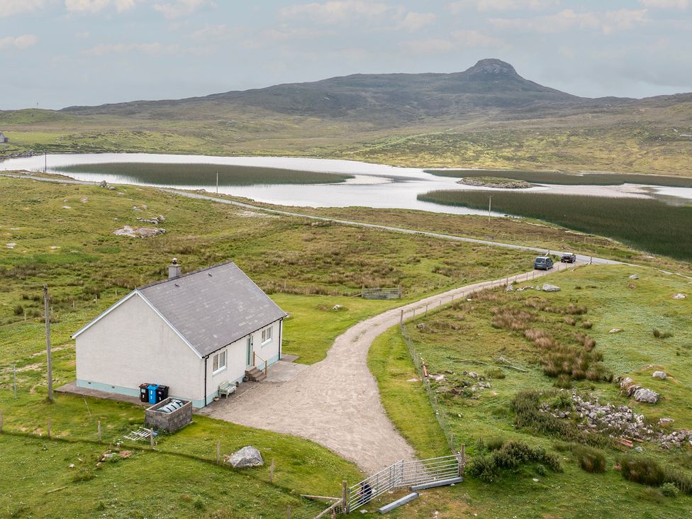 A house near a lake with a road and cars at Taigh Eva near Lochmaddy