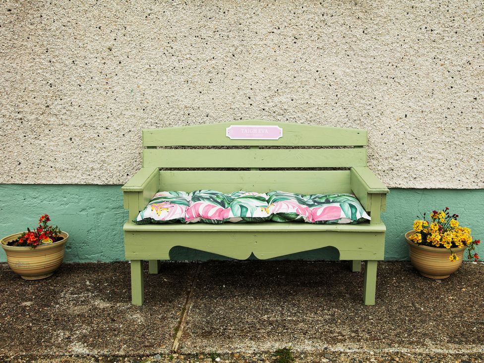 A green bench with cushions and flower pots at Taigh Eva near Lochmaddy
