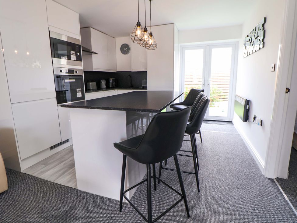 A kitchen with a counter and stools at 4 Willow Grove - Freehold Talacre