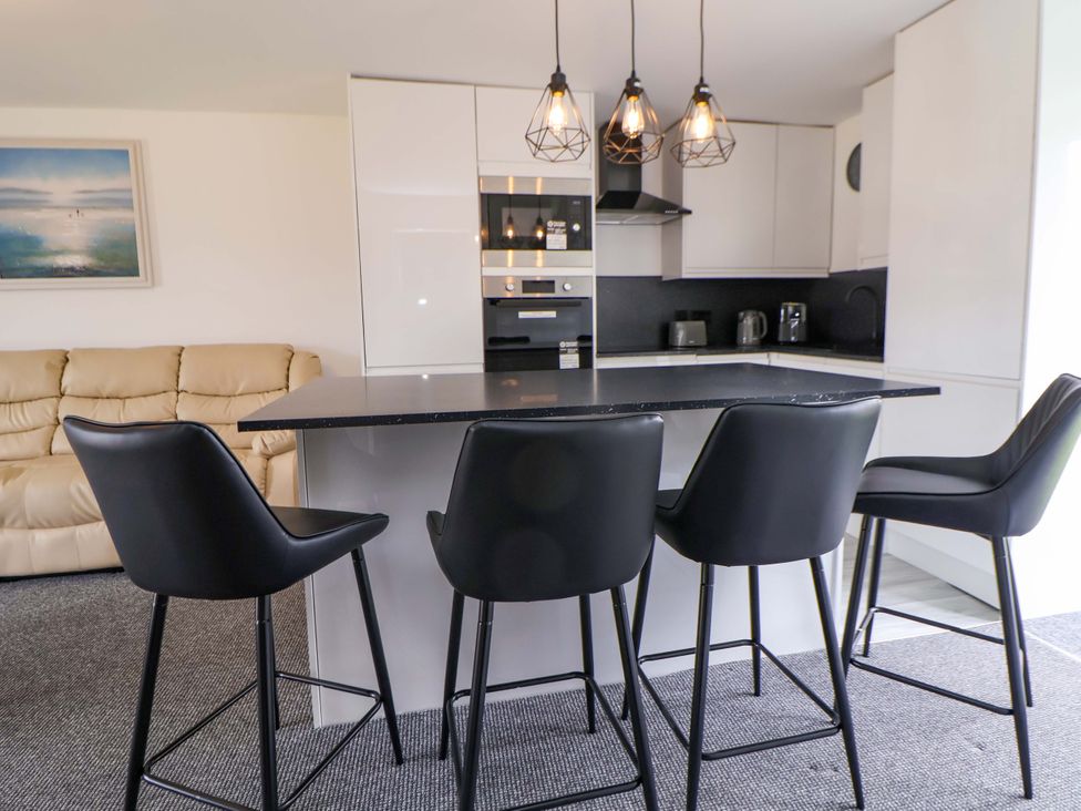 A kitchen with bar stools and appliances at 4 Willow Grove - Freehold in Talacre