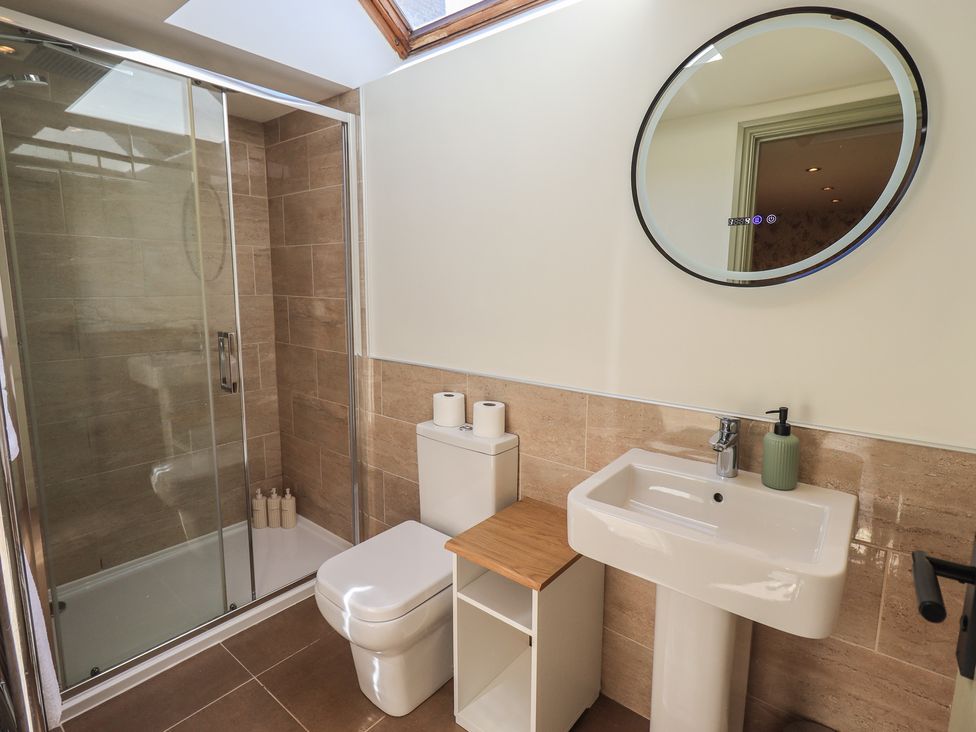 A bathroom with a shower, toilet, sink, and mirror at Fogga Croft in Gargrave