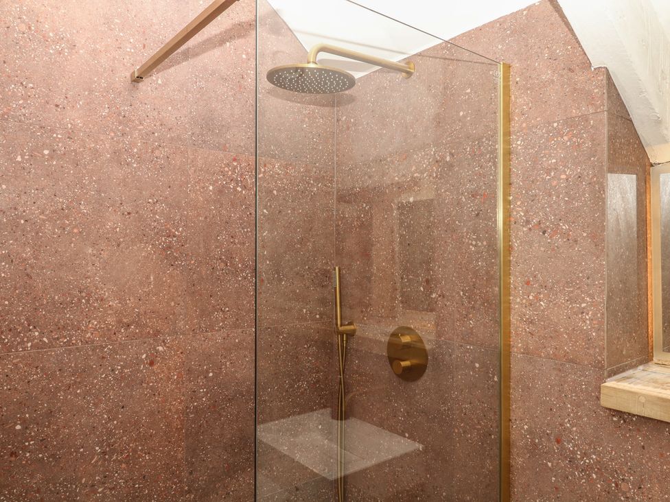 A shower with a glass panel and brass fixtures at Reddaway Threshing Barn near Okehampton