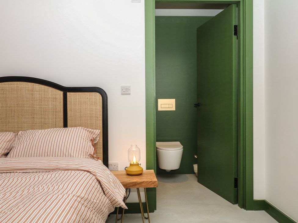 A bedroom with a bed and a green door leading to a toilet at Reddaway Threshing Barn near Okehampton