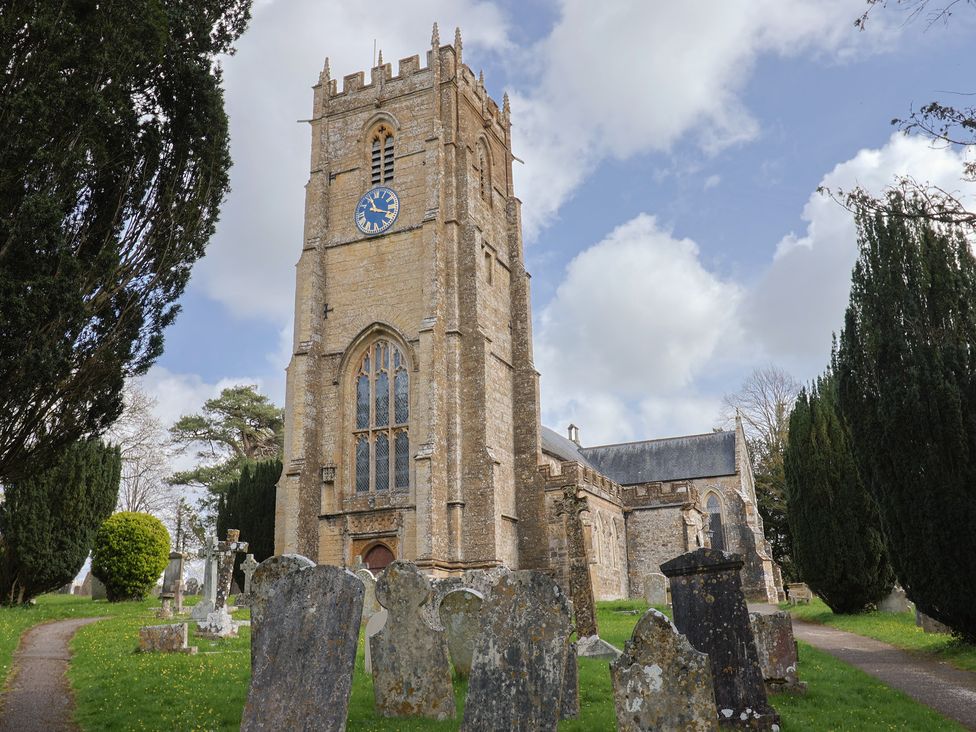 A church with a clock tower and grave stones along a pathway at Daisy Cottage Whitchurch Canonicorum near Charmouth