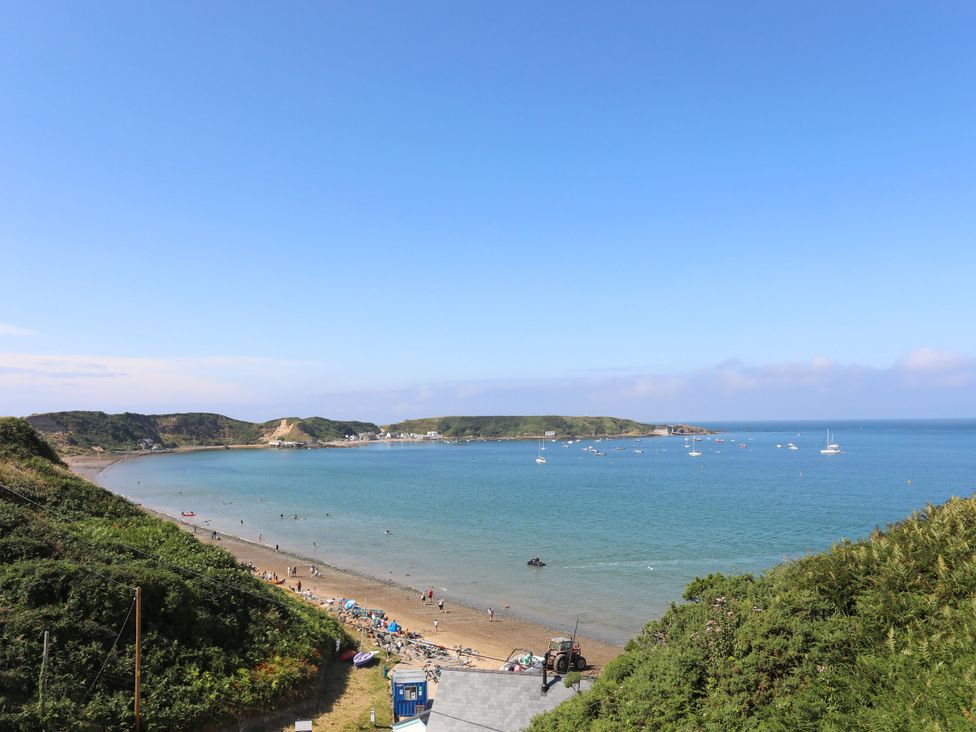 A coastal bay with boats anchored in the water and people on a beach at Pen-Y-Bont in Trefor