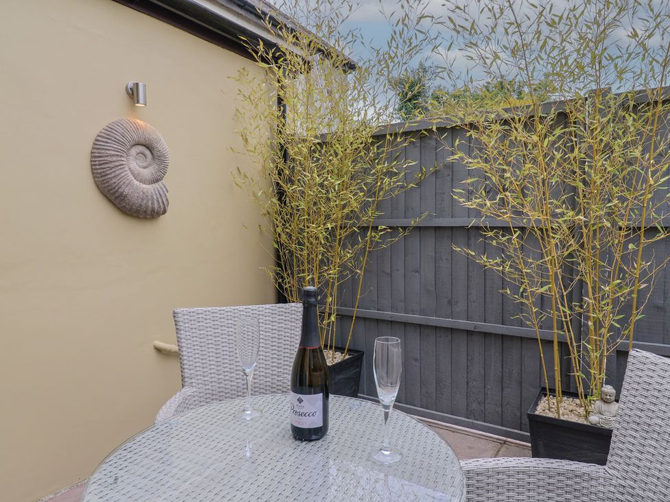 An outdoor seating area with a table, chairs, and a bottle of prosecco at Flat 2 The Cedars in Lyme Regis