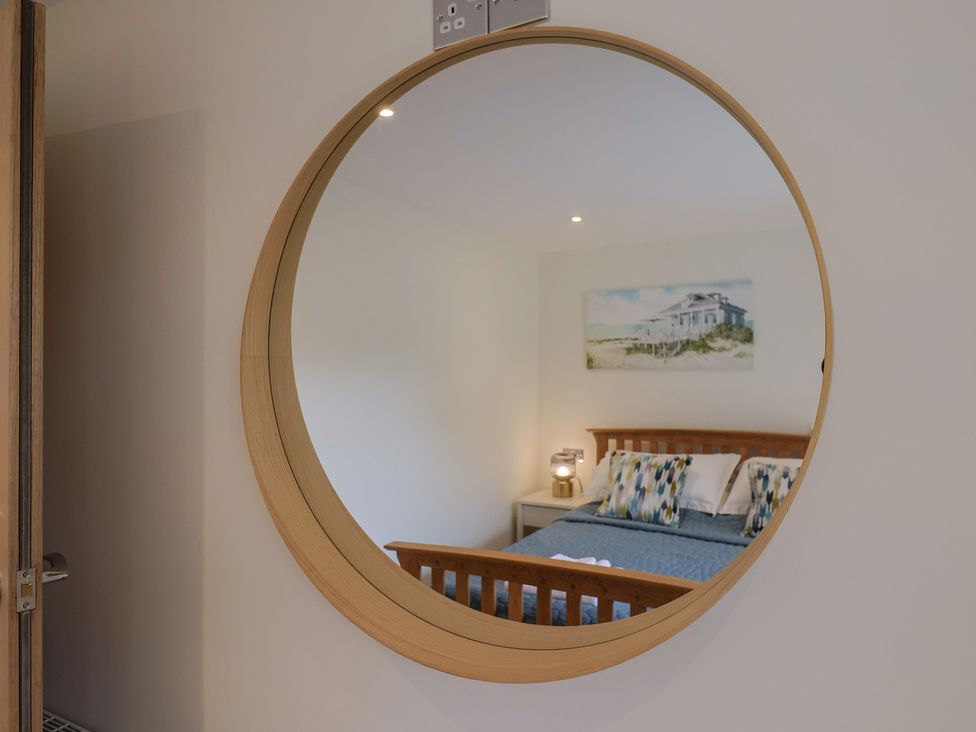A bedroom with a mirror reflecting a bed and lamp at Flat 2 The Cedars in Lyme Regis
