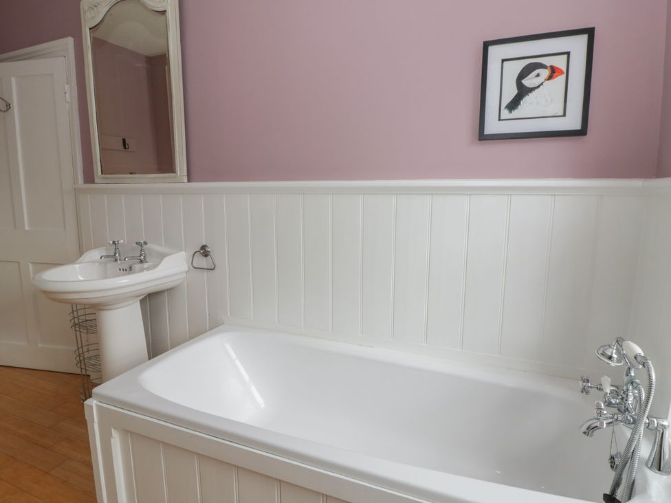 A bathroom with a bathtub, sink, and wall art at Ty Clyd in Newport, Pembrokeshire