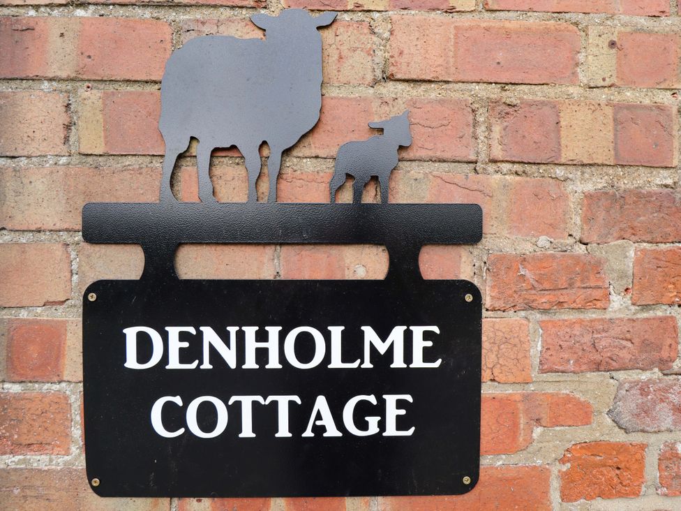 A sign featuring sheep and text at Denholme Cottage in Hogsthorpe