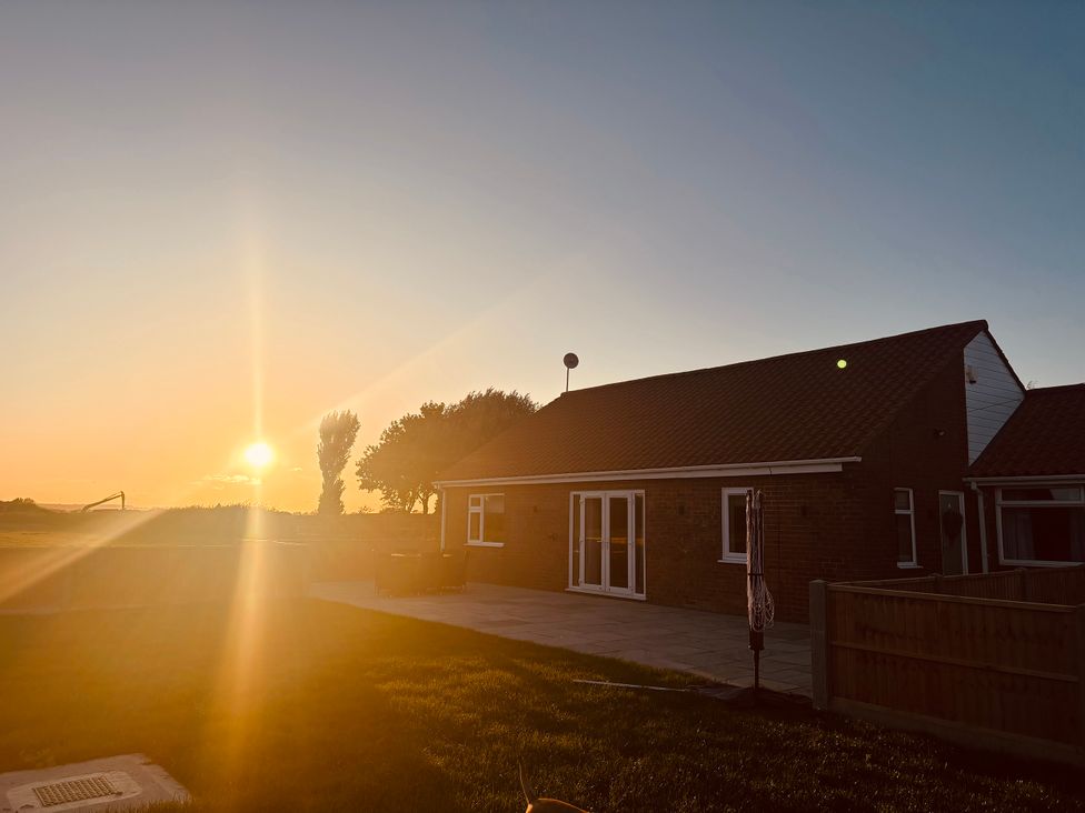 A house illuminated by sunset with a patio and grass at Denholme in Hogsthorpe