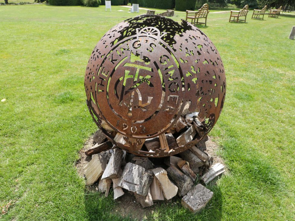 An iron sphere sculpture surrounded by wooden logs in a grassy area at The King's Ginger in Elcot near Kintbury