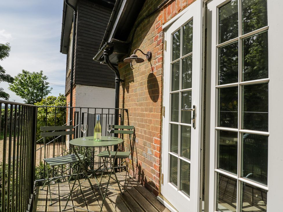 A small balcony with a round table and two chairs with a bottle and glasses near white French doors at Cedar in Elcot near Newbury