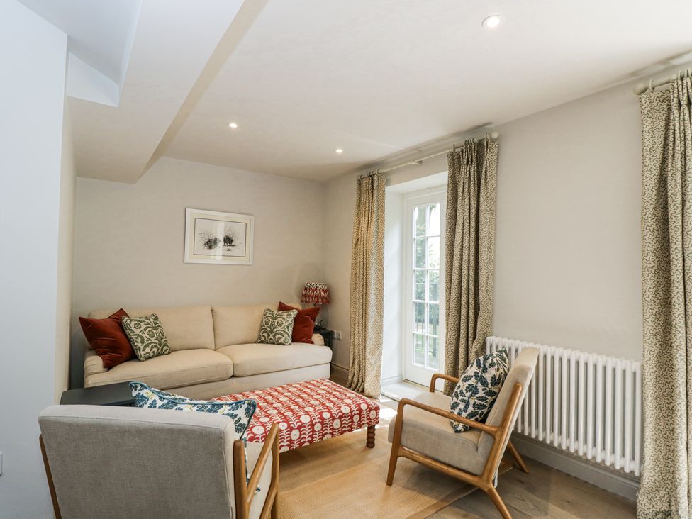 A living room with a beige sofa, two armchairs, a red patterned ottoman and curtains at Cedar in Elcot near Newbury