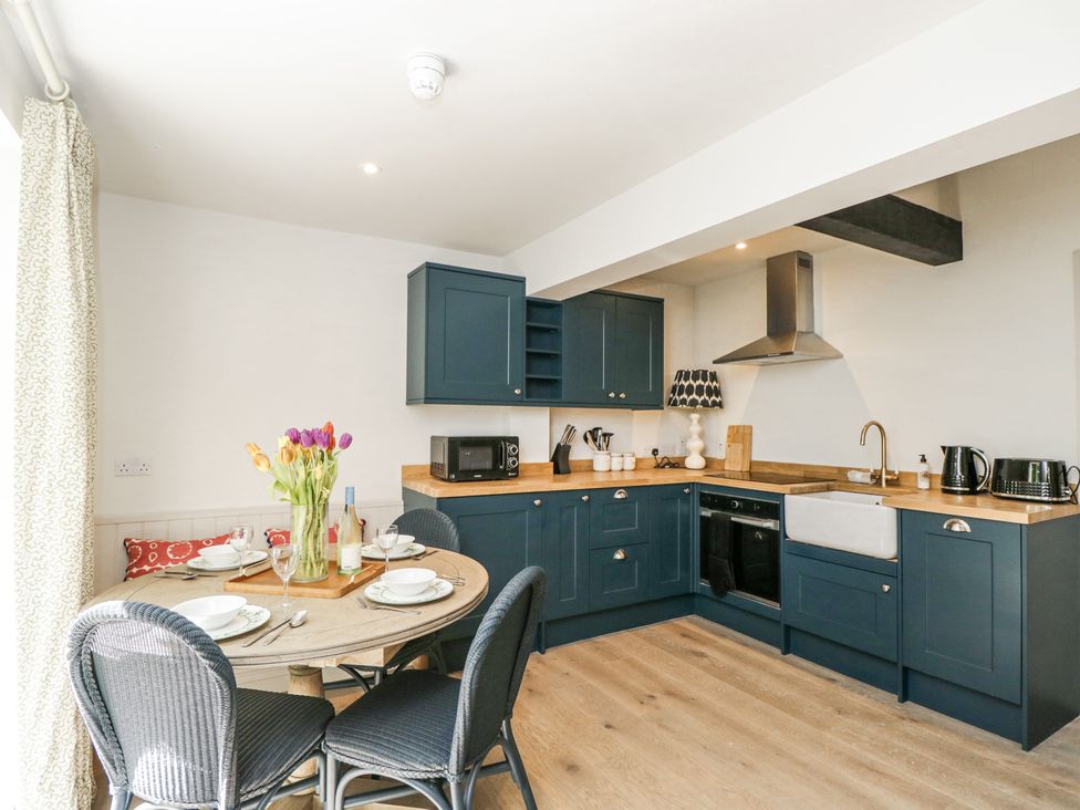 A kitchen with blue cabinets wooden countertops a round dining table with chairs and tulips at Cedar in Elcot near Newbury