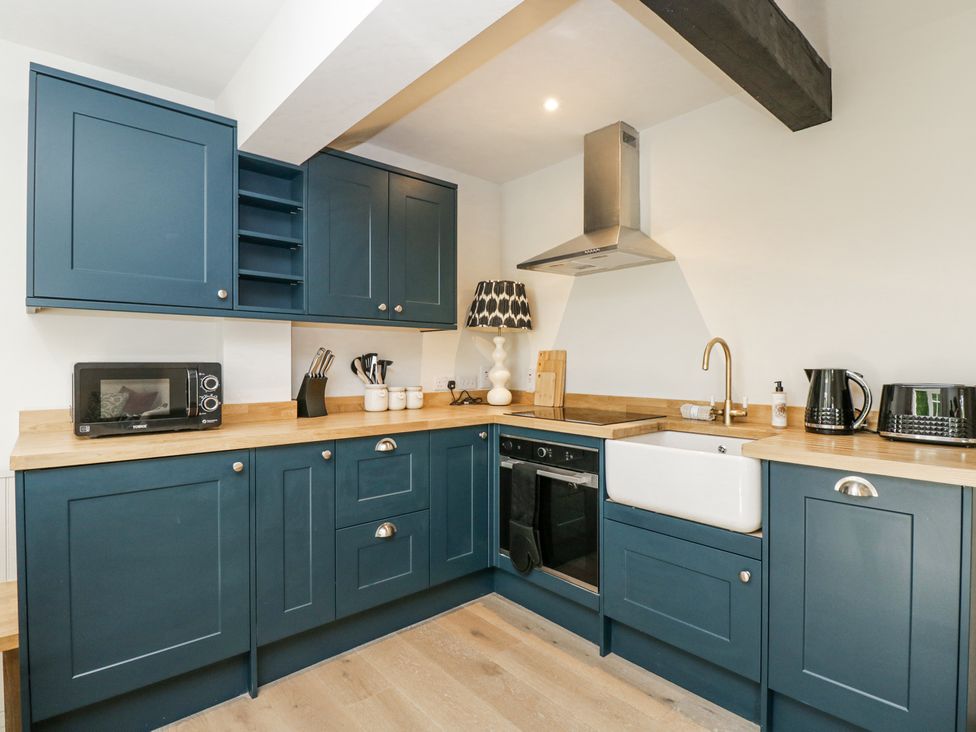 A kitchen with blue cabinets wooden countertops a white sink black microwave kettle toaster and cooking utensils at Cedar in Elcot near Newbury