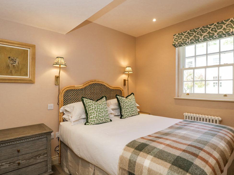 A bedroom with a bed with patterned pillows and blanket a window with a decorative blind and a wooden chest of drawers at Cedar in Elcot near Newbury